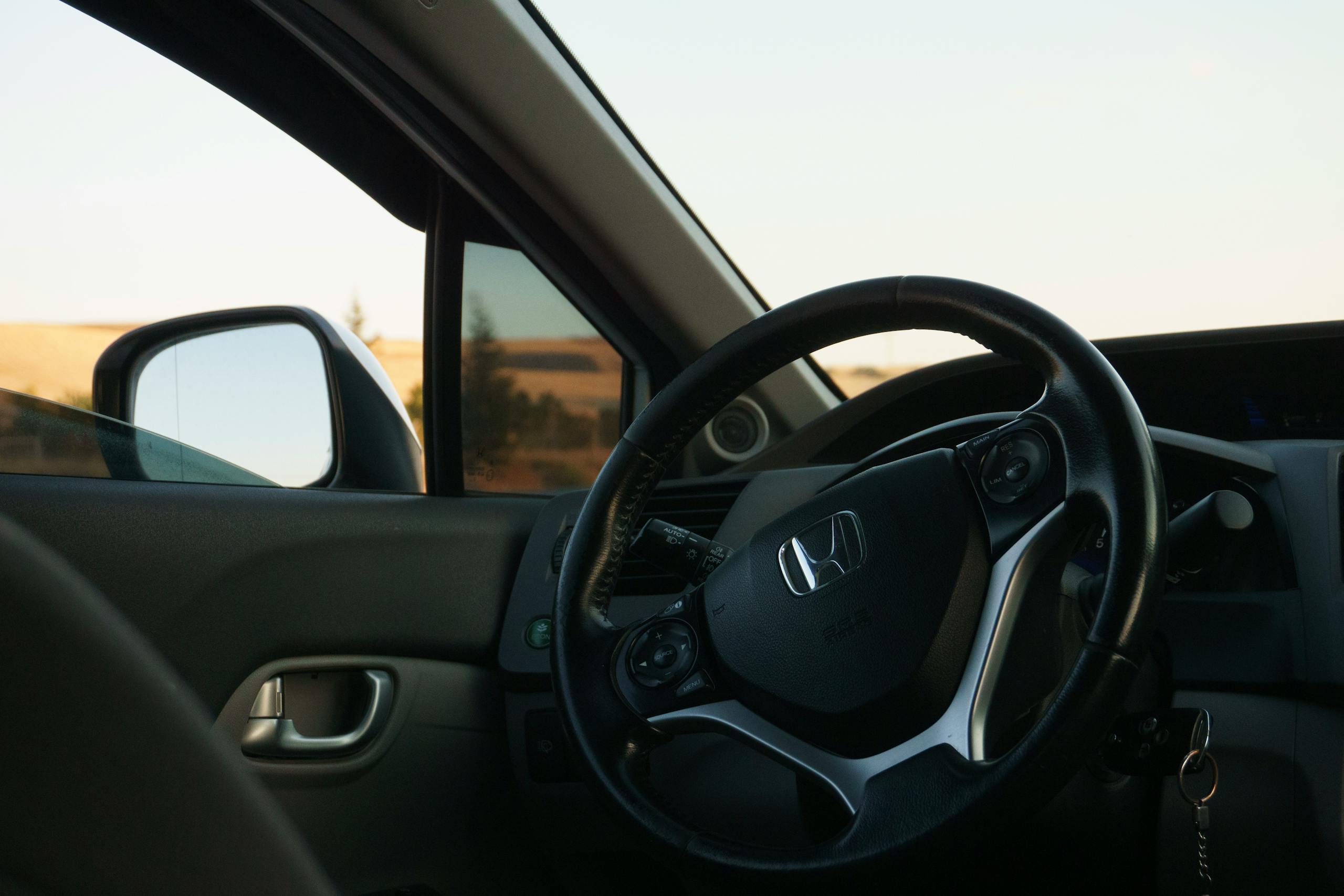 Close-up of a car steering wheel with dashboard and window view, embodying luxury and travel.